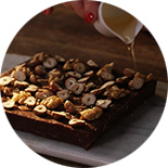 Gâteau brownie sur une planche en bois et une petite tasse qui fait couler du sirop d'érable 