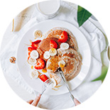 Pancakes dans une assiette blanche avec des fraises et bananes découpés en morceaux 
